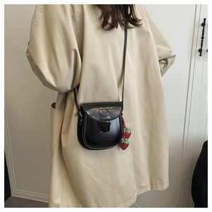 Mini borsa a sella nera con ciondoli a fragola su trench coat beige