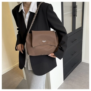 Close-up of the textured brown leather flap and stylish metal chain strap on the tote bag