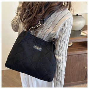 Detail of black quilted tote bag with gold chain strap on model in beige sweater