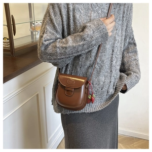 Detail of a brown vintage leather saddle bag with cute strawberry charms on a gray sweater