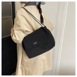 Detail view of the black leather shoulder bag with chain strap on a trench coat