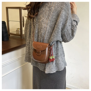 Mini borsa a sella vintage marrone con ciondolo fragola indossata su maglione grigio