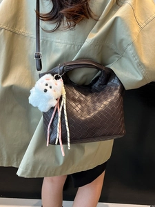 Dark brown woven leather handbag with plush charm and adjustable shoulder strap