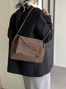 Brown leather tote bag with chain strap shown on a model in a minimalist setting