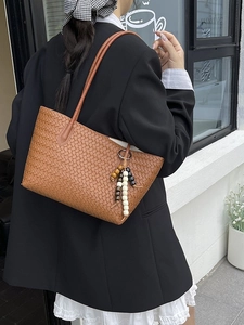 Brown woven leather tote bag with wooden bead charm on a shoulder-slung model