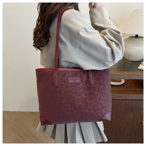 Detail der burgunderroten Tote Bag mit Leopardenmuster, getragen von einem Modell im Haus