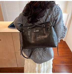 Detail of vintage black PU leather shoulder bag worn over a gray knit sweater