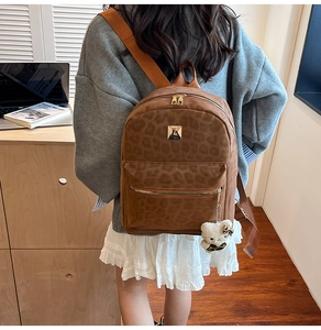 Detail view of leopard print backpack with gold zipper and plush bear charm decoration