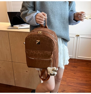Close-up of leopard print backpack featuring metal zippers and a plush bear pendant