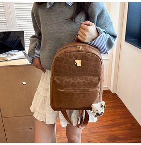 Detail of leopard print backpack texture with golden zipper and plush bear charm