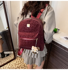 Detail of burgundy leopard print backpack with plush cartoon charm and metal logo plate