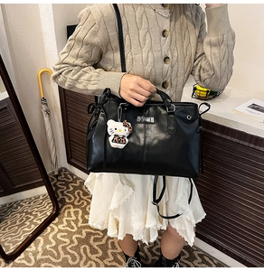 Detail of black faux leather tote bag with smooth texture and cute plush charm pendant
