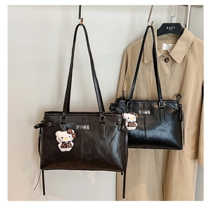 Detail of dark brown and black faux leather tote bags with metal logos and plush charms
