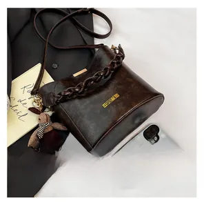 Detail of dark brown bucket bag with woven handle, gold logo and bear charm