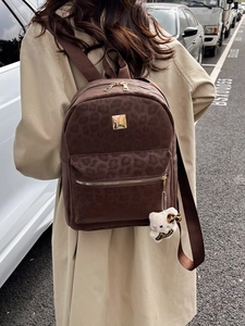 Outdoor back view of a dark brown leopard print backpack with gold hardware and plush charm