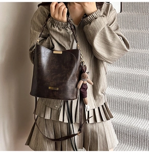 Close-up of vintage brown bucket bag with woven handle and plush bear charm detail