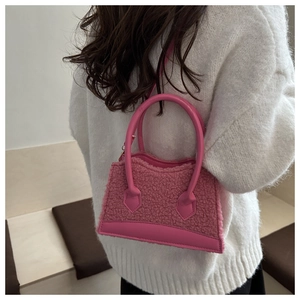 Detail view of pink fuzzy shearling handbag with leather trim held by a model in sweater