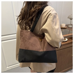 Detalle de bolso tote bicolor con textura de ante y placa de metal triangular con logo