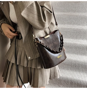 Detail of vintage dark brown bucket bag with woven handle and gold plaque on stairs