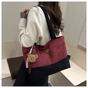Détail du sac cabas en daim bordeaux avec logo doré et accessoire d'ours en peluche