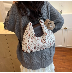 Detail of a white quilted tote bag with teddy bear patterns and a plush bear charm