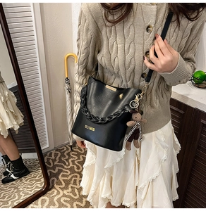 Close-up of black bucket bag with woven chain, long strap and cute bear charm