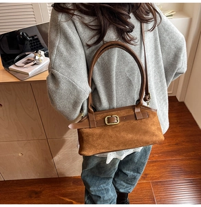 Detail of a brown suede shoulder bag with belt buckle on a warm indoor lifestyle background