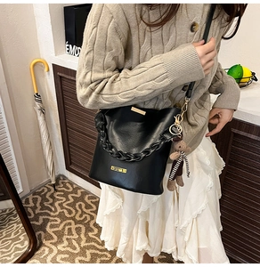 Detail of black leather bucket bag with chunky chain handle and cute bear charm