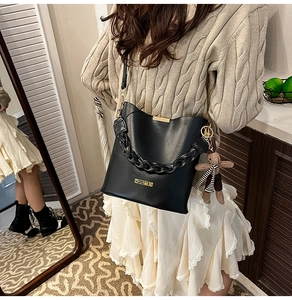 Detail of black bucket bag featuring woven chain design and striped bear charm