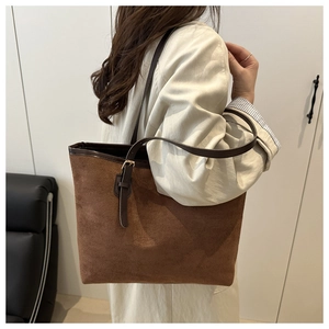 Detail of a brown suede tote bag featuring a leather strap and gold-tone metal buckle