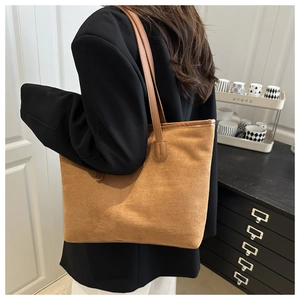 Détail du sac cabas en daim caramel porté à l'épaule dans un décor moderne