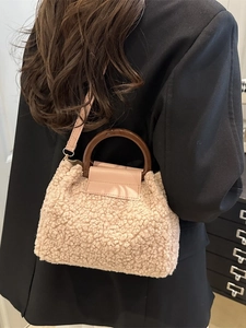 Beigefarbene Plüsch-Handtasche mit Holzgriffen, getragen von einem Model im Sakko