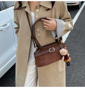 Brown suede baguette shoulder bag with decorative leather strap and plush charm