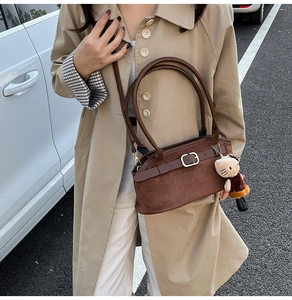 Close-up of brown suede handbag with leather straps, metal buckles and plush charm