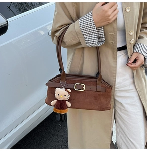 Detail of a brown suede hobo bag with leather strap and plush cat charm on side