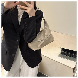 Detail of a chic beige patent leather dumpling bag with decorative buckle on model