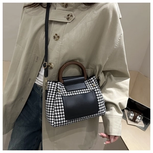 Houndstooth crossbody bag with round wooden handle and leather strap on model in trench coat