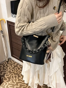 Chic black PU leather bucket bag with woven handle and cute bear charm worn by a model