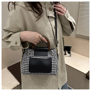 Detail of houndstooth crossbody bag with retro wooden handle and black leather pocket