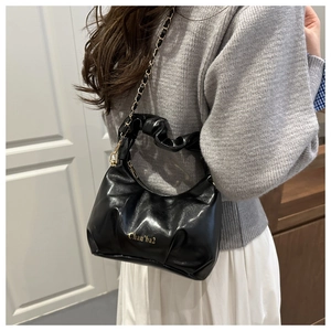 Detail of black glossy pleated handbag with golden chain strap and brand lettering