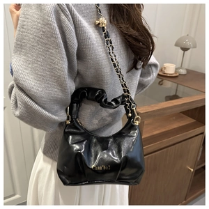 Detail of glossy black leather crossbody bag with gold chain and adjustment ball buckle
