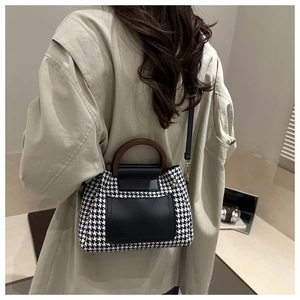 Detail of classic houndstooth crossbody bag with elegant wooden handle and black leather flap