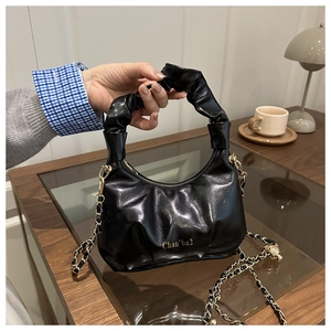 Detail of glossy black pleated handbag with scrunchie handle and gold chain strap