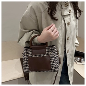Detail of houndstooth crossbody bag with brown leather accents on a beige coat outfit