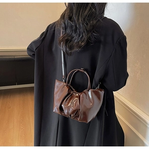 Brown pleated cloud bag with shiny finish worn by a model in a black blazer