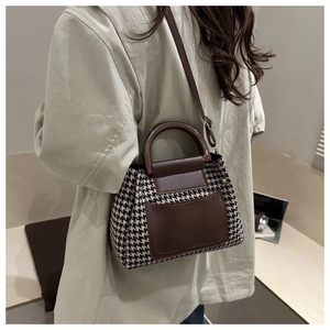 Detail of vintage houndstooth handbag with brown leather strap worn on shoulder