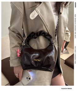 Detailed view of dark brown glossy leather bag with pleated handle and metal chain strap
