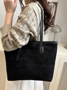 Minimalist black suede tote bag shown on a model in a warm indoor home setting