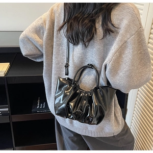 Rear view of model wearing a black glossy pleated cloud bag with adjustable crossbody strap