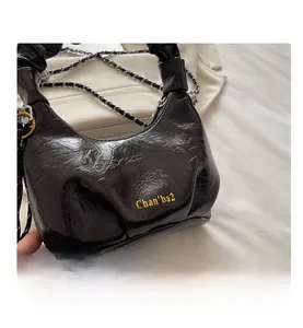 Close-up of black pleated glossy leather bag with silver chain and gold logo detail